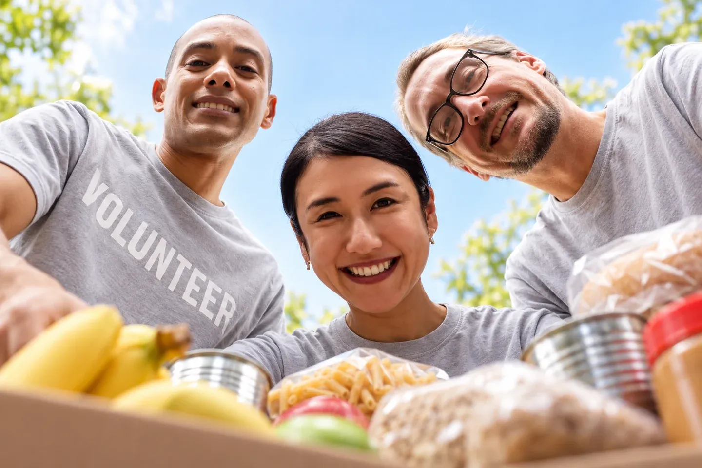 Three smiling volunteers gathered around a box of donated groceries